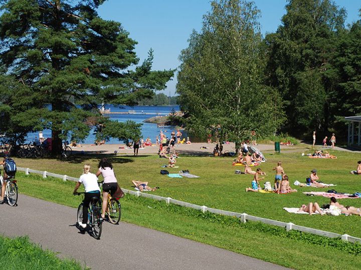 Myllysaaren pikniknurmella on paljon ihmisiä helteisenä päivänä, pyörätiellä kulkee pyöräilijöitä